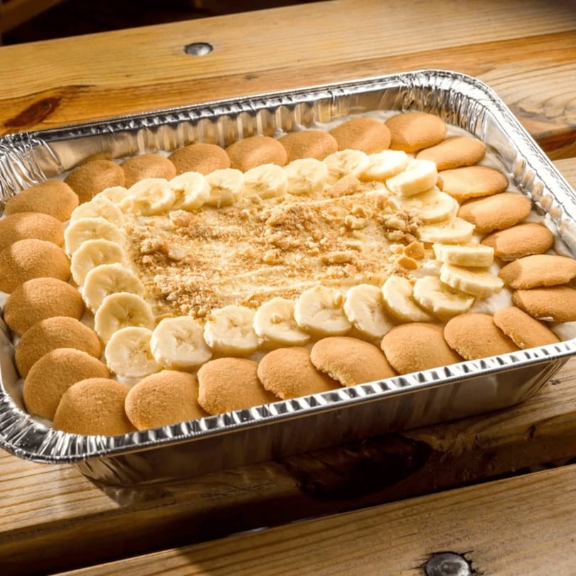 A large aluminum pan of Annie O's Kitchen's banana pudding with vanilla wafers and sliced bananas.